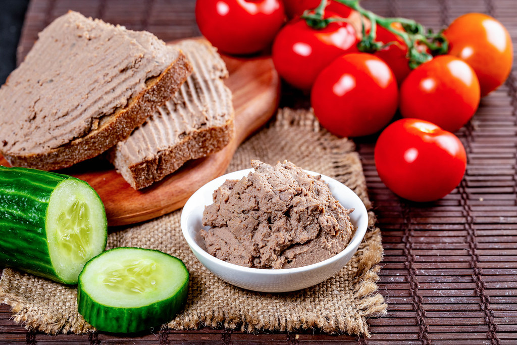 Delicious pate in a bowl and on sandwiches on the table with tomatoes and cucumbers